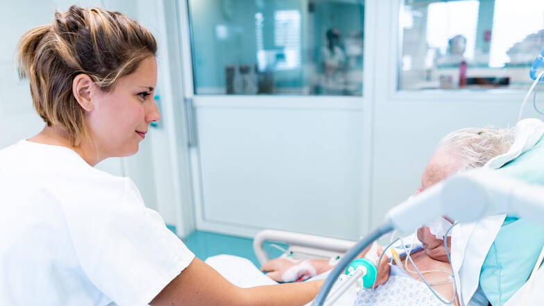 Une infirmière ajuste ajuste un tuyau de perfusion passant sur le torse d'un patient et lui sourit. 