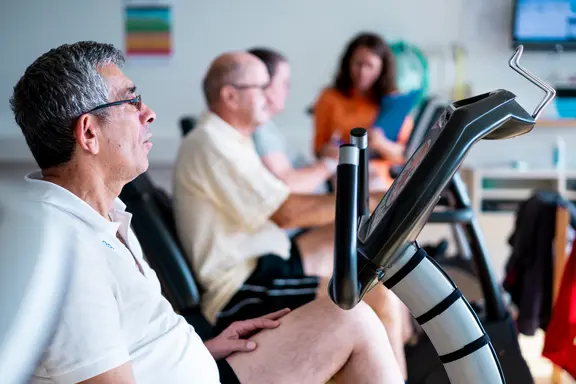 Des patients s'entraînent sur des vélos d'intérieur, sous la supervision d'une physiothérapeute